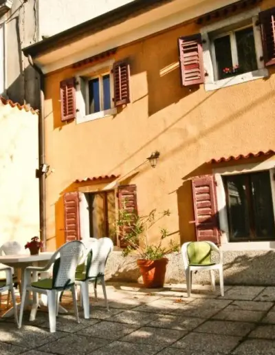 Una casetta con un piano, illuminata dal sole con piccole finestrelle. Fuori un tavolino con delle sedie con cuscini morbidi.